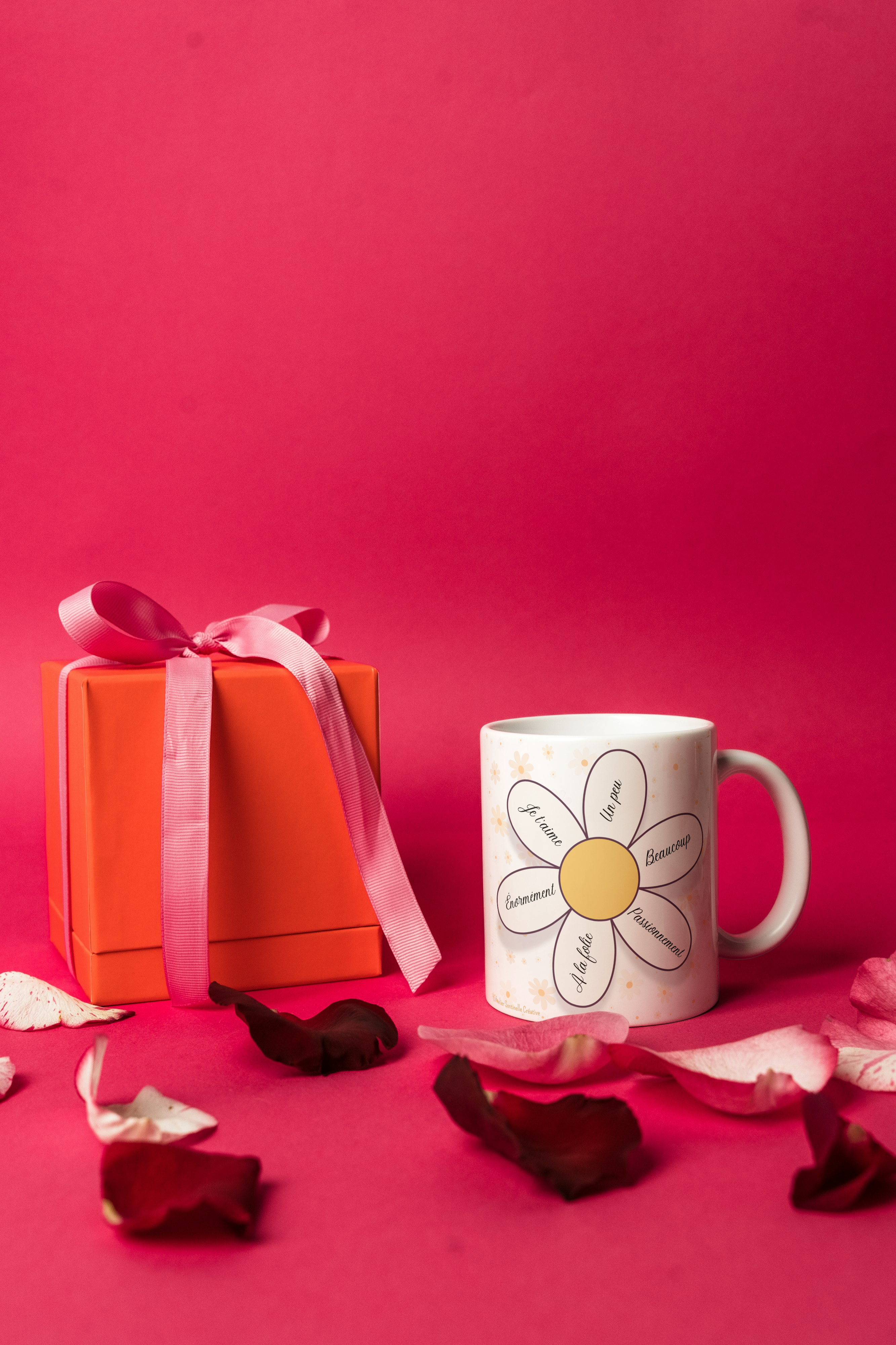 Mug blanc à motif marguerite, posé près d’un coffret cadeau, anse visible