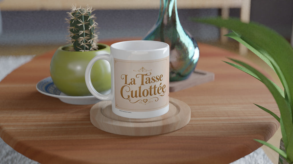 Mug blanc sur dessous de bois avec inscription « La Tasse Culottée ».